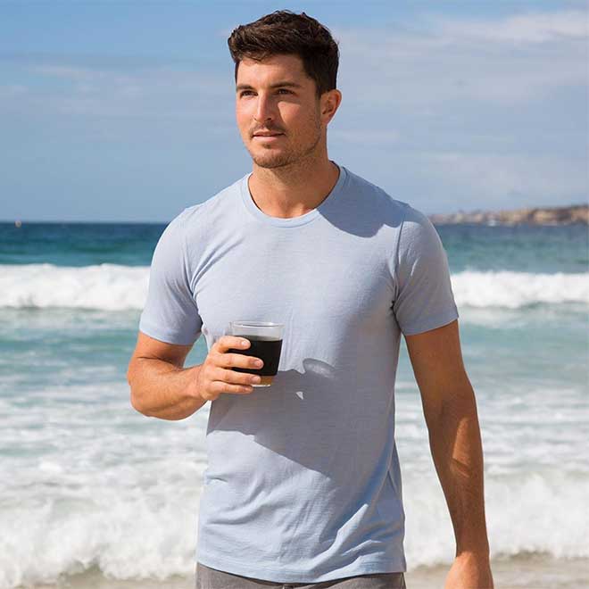 Man standing at the beach wearing a blue icebreaker Tech Lite t-shirt